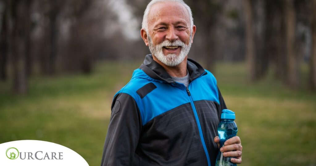 An older man smiles with a water bottle while exercising, representing the benefits of encouraging exercise when caring for seniors at home.
