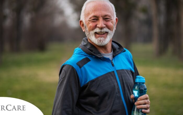 An older man smiles with a water bottle while exercising, representing the benefits of encouraging exercise when caring for seniors at home.