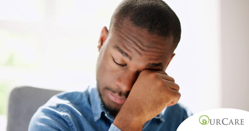 A man tiredly rubs his eyes, representing the exhaustion that can come with family caregiving.
