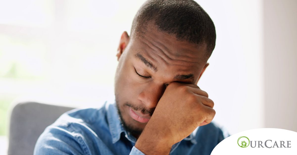 A man tiredly rubs his eyes, representing the exhaustion that can come with family caregiving.