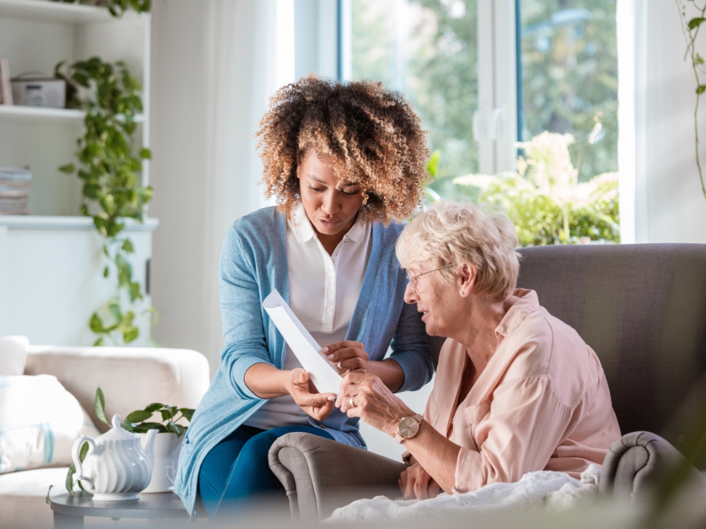 A caregiver sits next to an elderly woman helping her to read a letter. Personalized Senior Home Care in Bloomingdale, Florida.