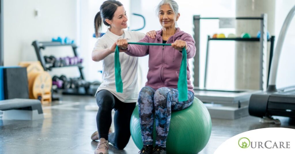 A care provider helps an older woman exercise with a resistance band and an exercise ball, representing how exercise can help with senior fall prevention.