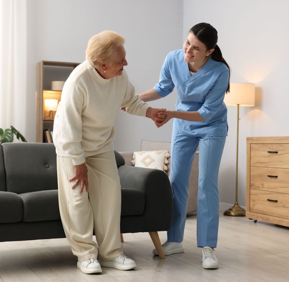 A caregiver assisting an elderly woman with standing up safely from a chair, providing hands-on support during mobility care in a comfortable home setting in Temple Terrace.