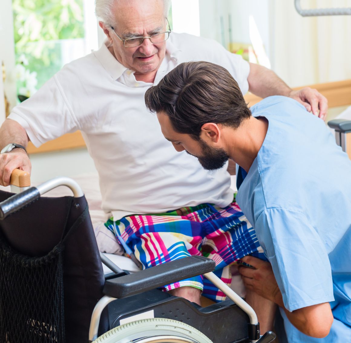 A caregiver assisting an elderly man with transferring from a bed to a wheelchair, providing safe mobility support as part of home care in Temple Terrace.